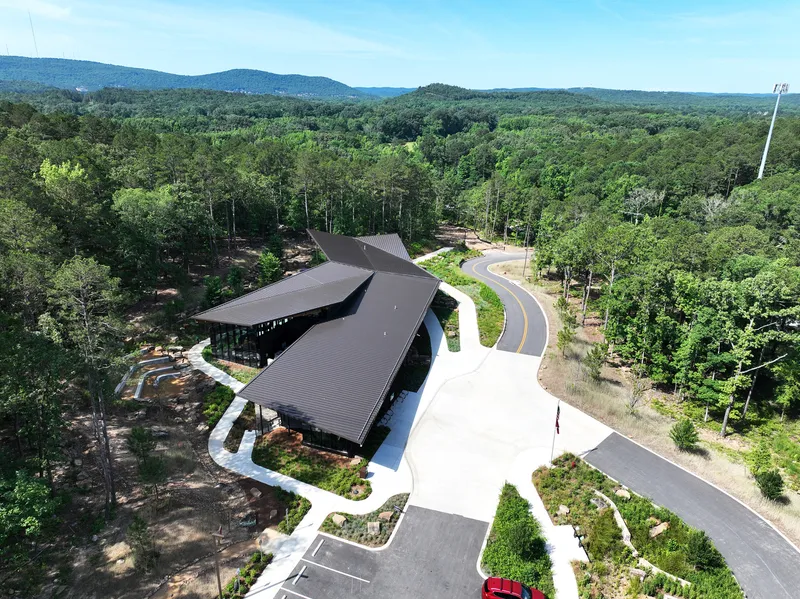 Drone view of the folded roof nestled among forested hills and curving access road