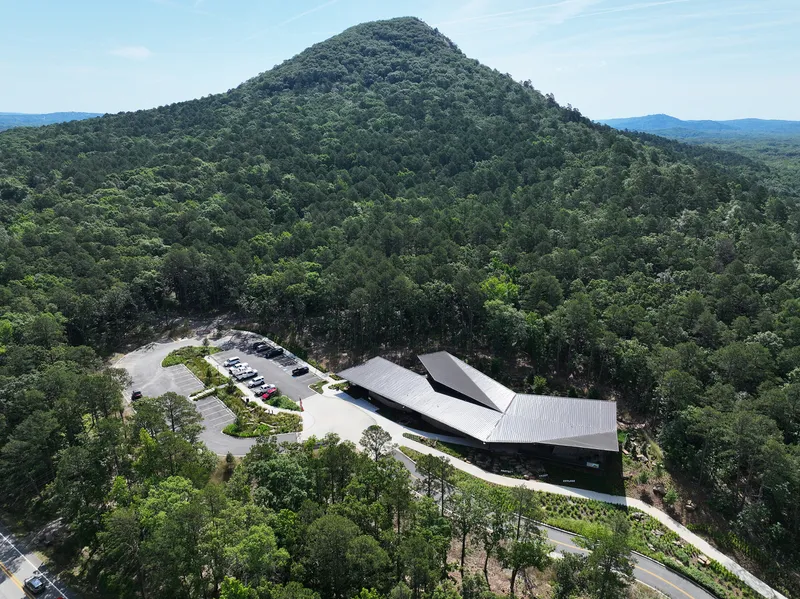 Aerial view of the three-lobed metal roof building nestled at the base of a forested mountain