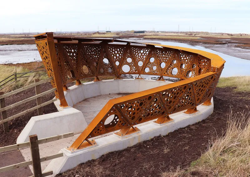 Angular observation deck with rusted steel screens and concrete seating bench beside marshland