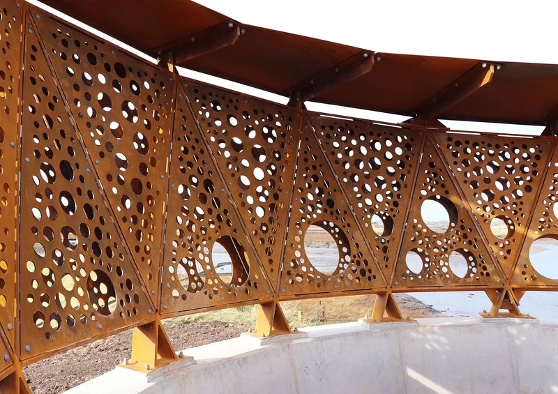 Interior view of perforated weathering steel panels with exposed roof beams framing the wetland beyond