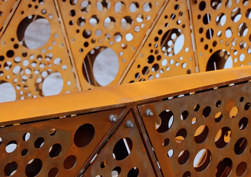 Close-up of bolted steel connections on the perforated orange metal screening panels