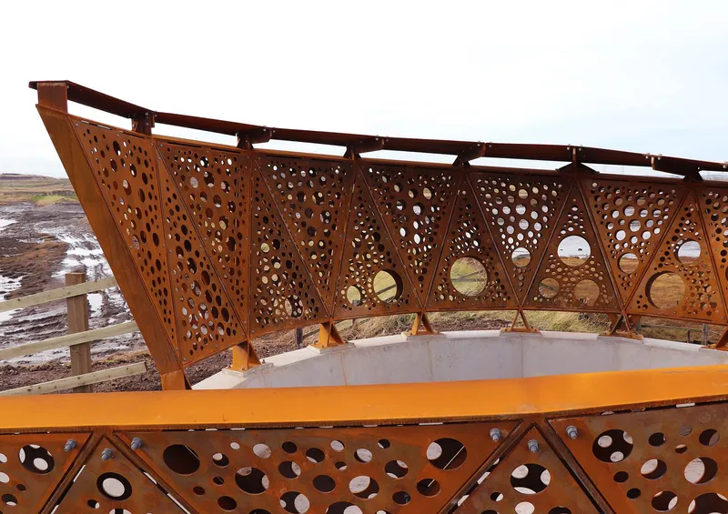 Weathered steel viewing platform with perforated screens and triangular bracing overlooking a tidal landscape