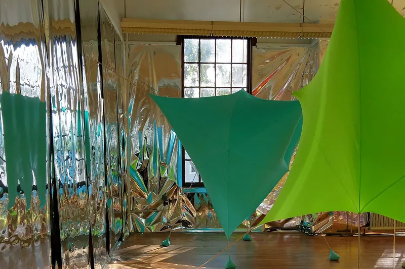 Interior installation with green and teal tensile fabric canopies suspended above reflective foil panels
