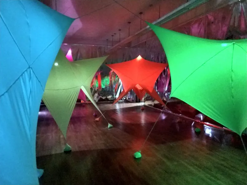Tensioned fabric structures in red, yellow, green and blue creating passageways over polished wooden flooring