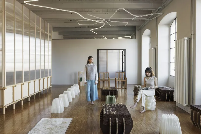 Interior studio with translucent timber-framed screen dividing a wooden floor beneath custom ribbon light fixtures