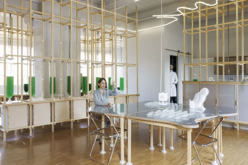Interior laboratory space with a wooden gridded shelving system displaying green glass vials and researchers at work