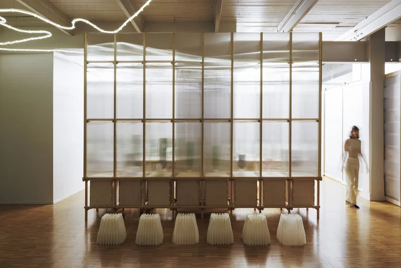 Freestanding translucent screen with timber frame and ribbed ceramic vessels lined up beneath on wood flooring