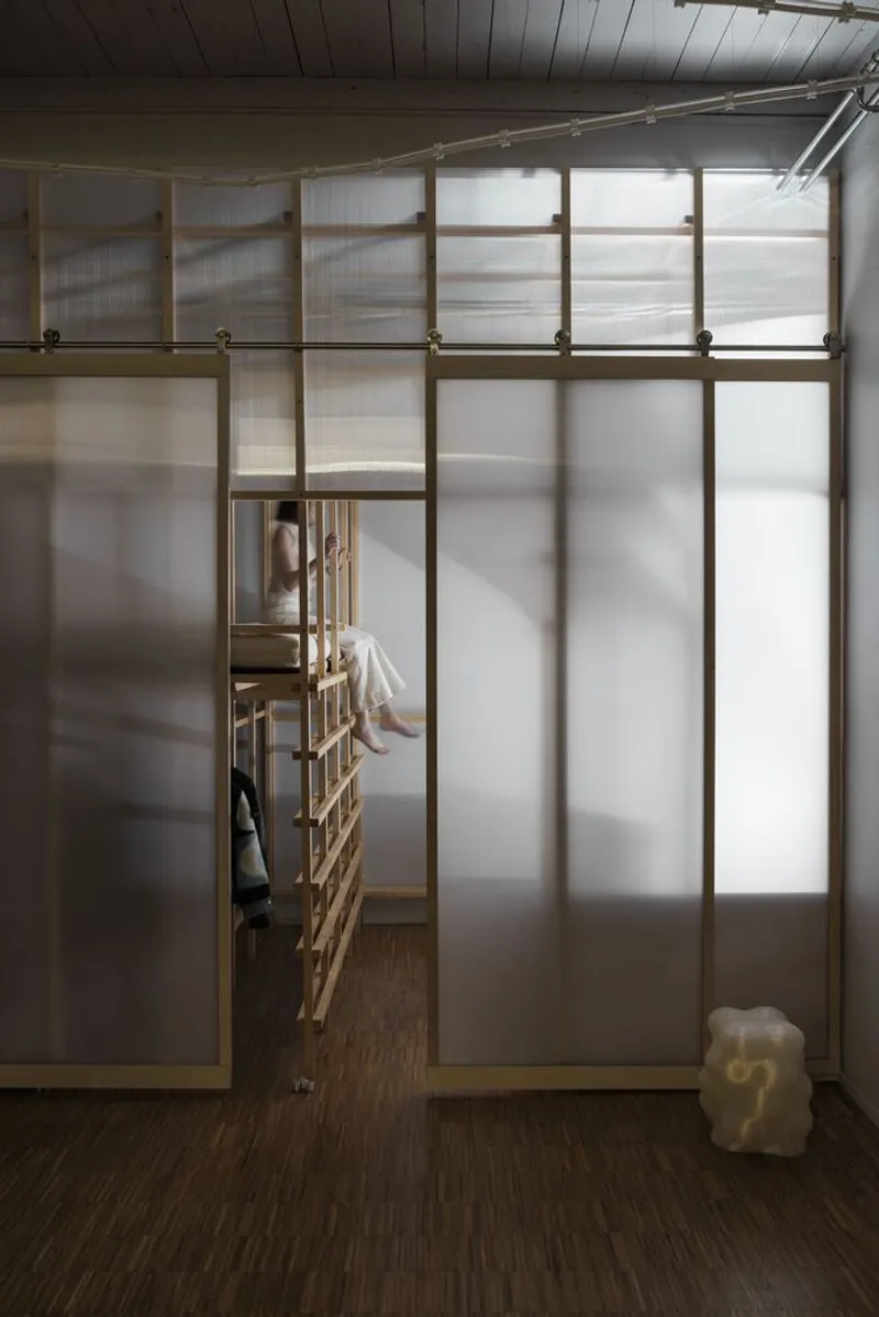 View through a translucent panel partition revealing a researcher seated on a wooden ladder