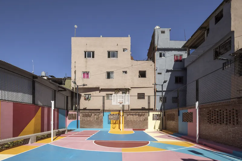 Multicolored basketball court wedged between low-rise residential buildings under a clear blue sky