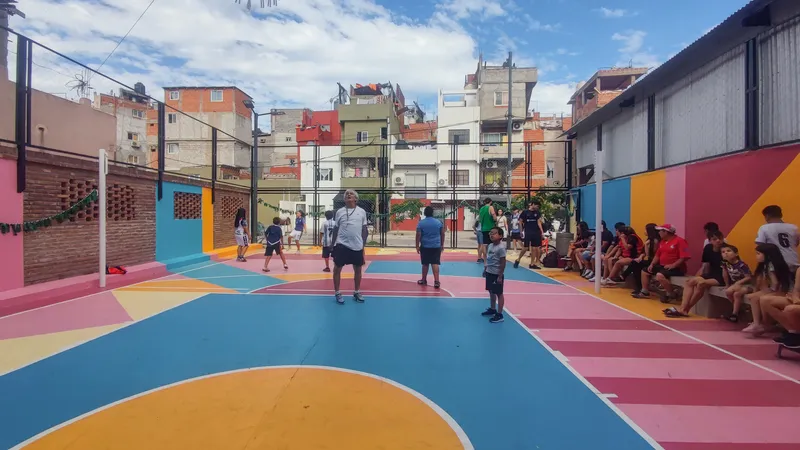 Children playing basketball on the painted court with spectators seated along the side wall