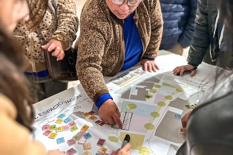 Community members gathered around a table reviewing site plans and architectural drawings during a workshop