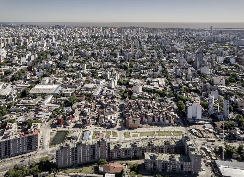 Wide aerial view showing an informal neighborhood amid the surrounding urban blocks and green spaces