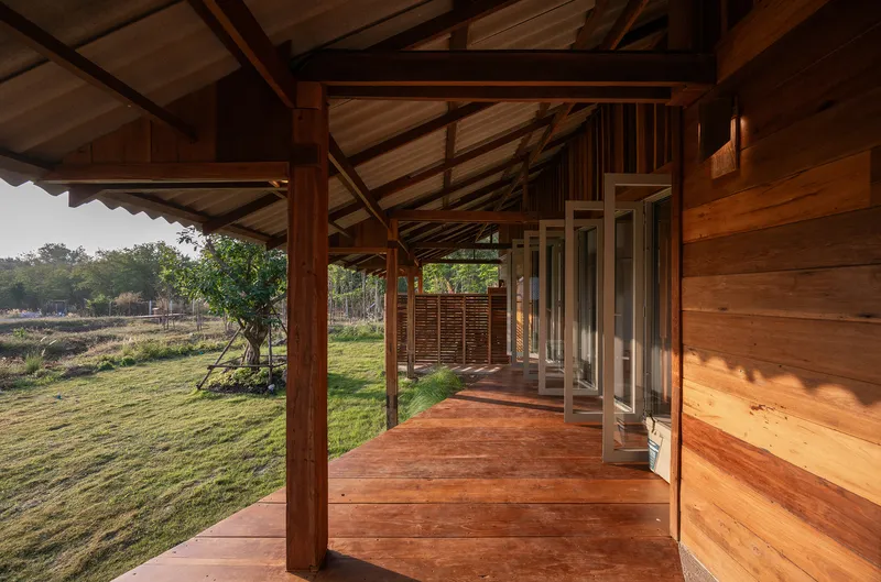 Covered timber walkway with exposed rafters and sliding glass doors overlooking grassy field