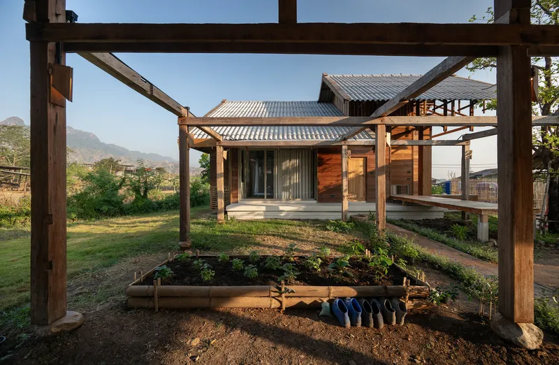 Timber entry pavilion framed by a pergola structure with planted beds and shoes below