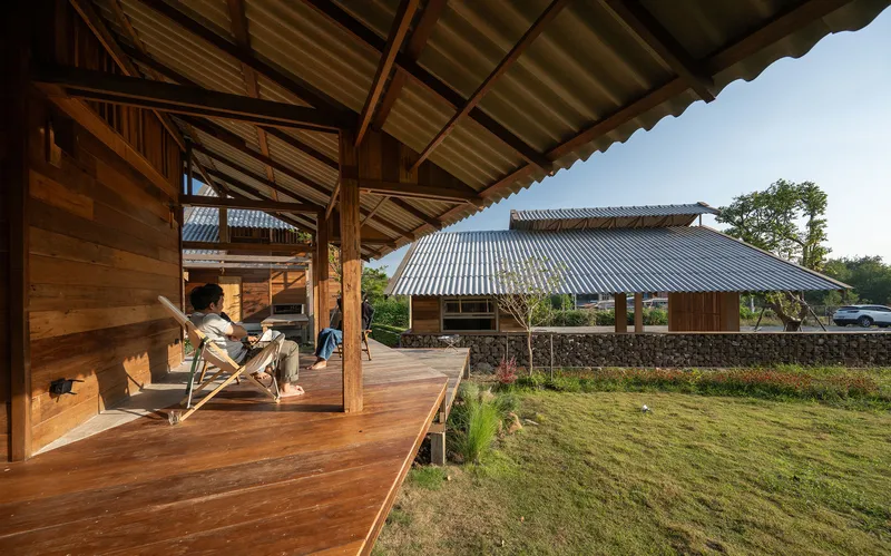 Timber veranda with truss structure and deck chairs opening onto a lawn and stone wall compound