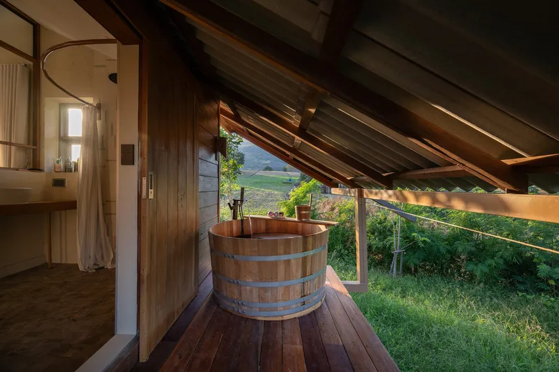 Wooden soaking tub on a private balcony under sloped rafters with views of distant hills