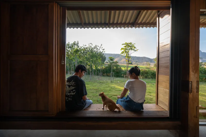 Two people and a dog sitting in a timber-framed doorway looking out to a landscaped lawn