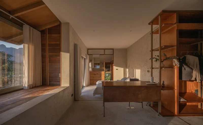 Interior bedroom with concrete platform bed and timber shelving bathed in afternoon sunlight