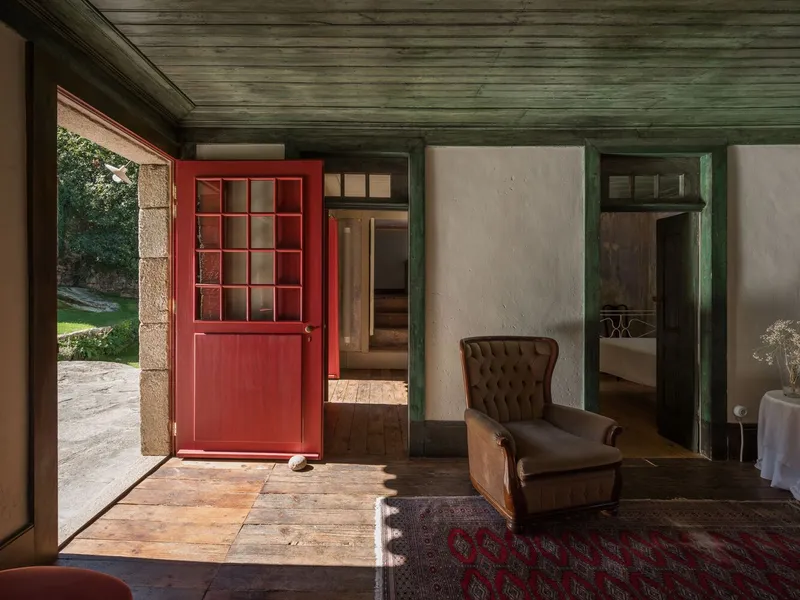 Interior threshold with open red gridded door leading to a stone courtyard in afternoon light