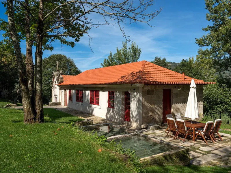 Low-slung stone and white stucco pavilion with orange tile hip roof and shallow pool terrace