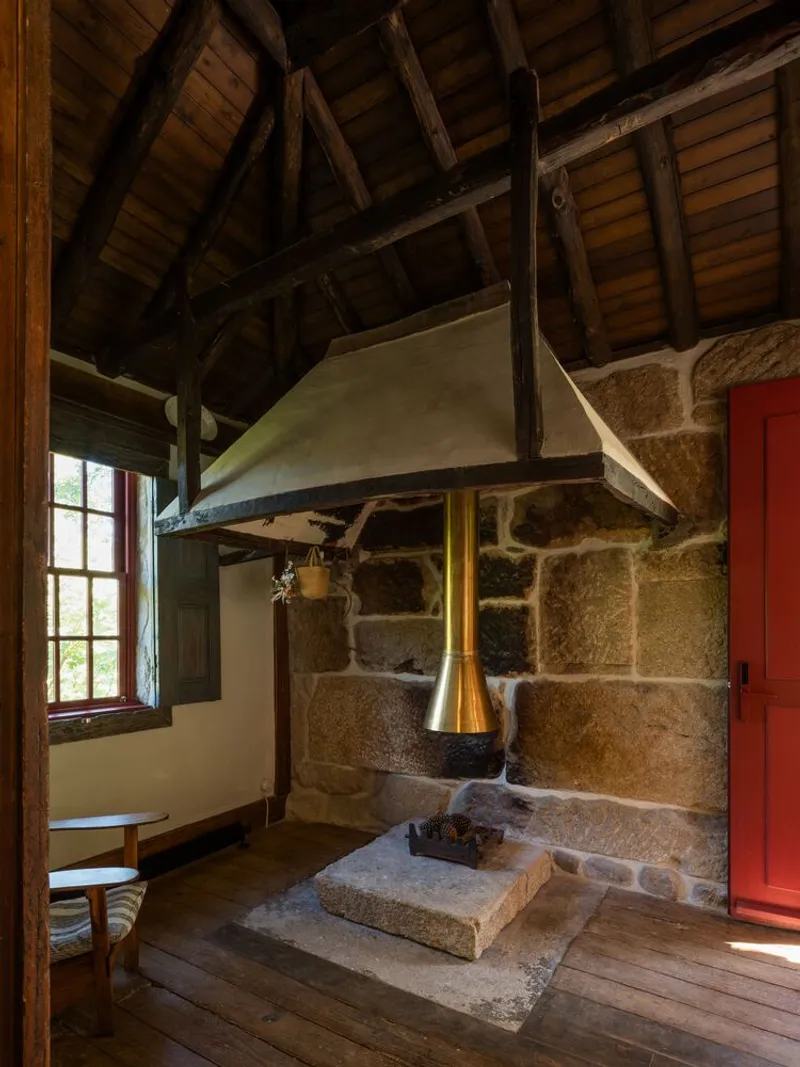 Interior hearth with stone base and white plaster hood beneath exposed timber roof beams and boarding