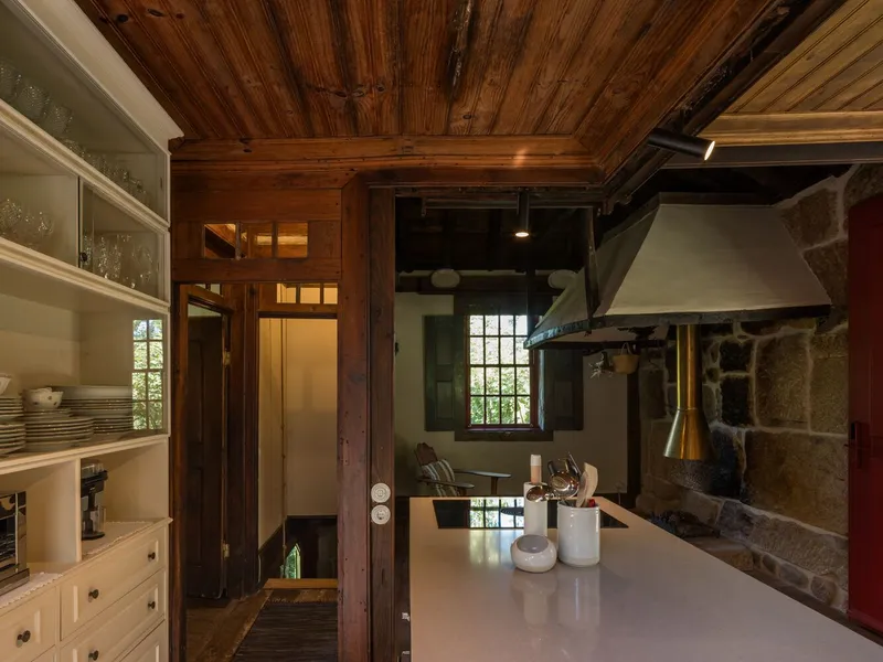 Kitchen with white cabinetry and central island beneath timber plank ceiling and stone fireplace hood
