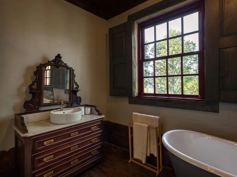 Bathroom with gridded window framing green foliage and freestanding tub beside vintage vanity