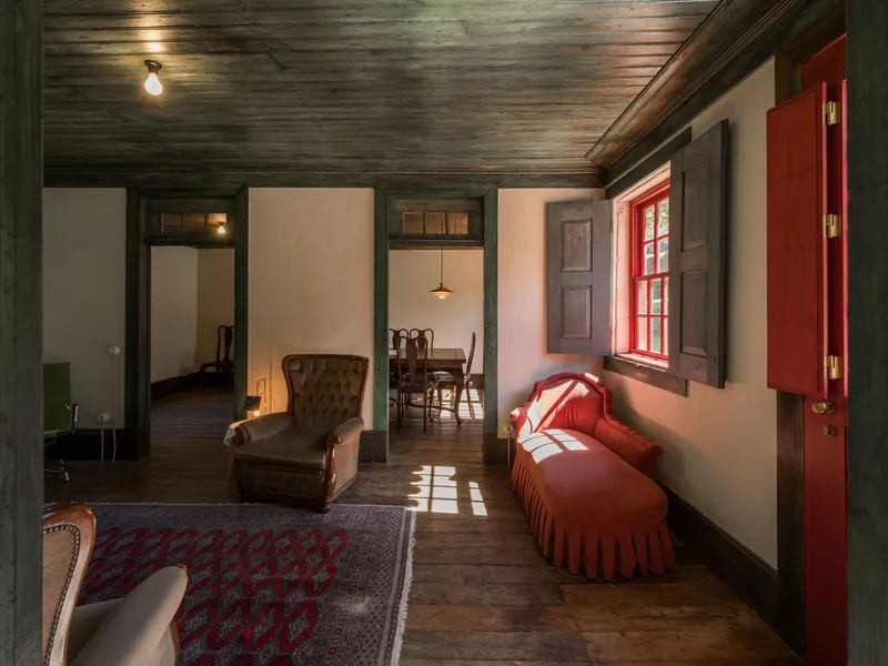 Living space with dark timber ceiling and red chaise beneath window casting afternoon sunlight