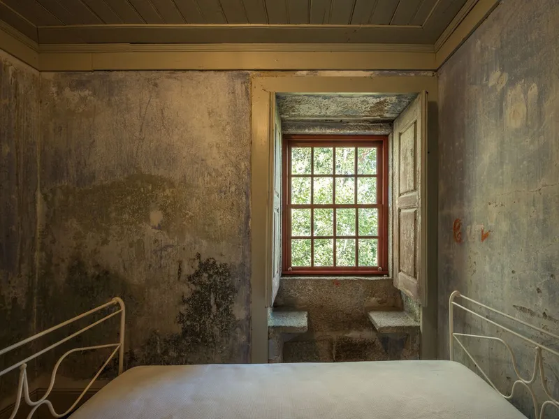 Bedroom with distressed plaster walls and deep window alcove looking onto trees