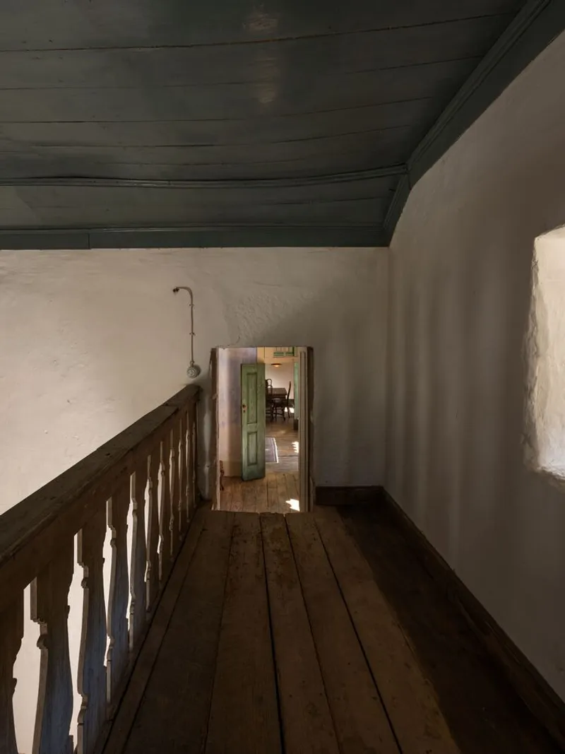 Timber balustrade along a narrow hallway with whitewashed walls and dark stained ceiling boards