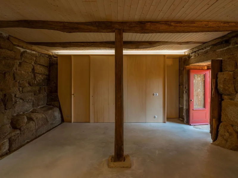Interior room with plywood partition walls flanked by granite masonry and timber post on concrete floor