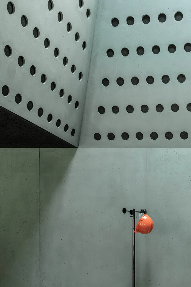 Perforated concrete panels meet smooth concrete base with orange task lamp casting shadows at the junction