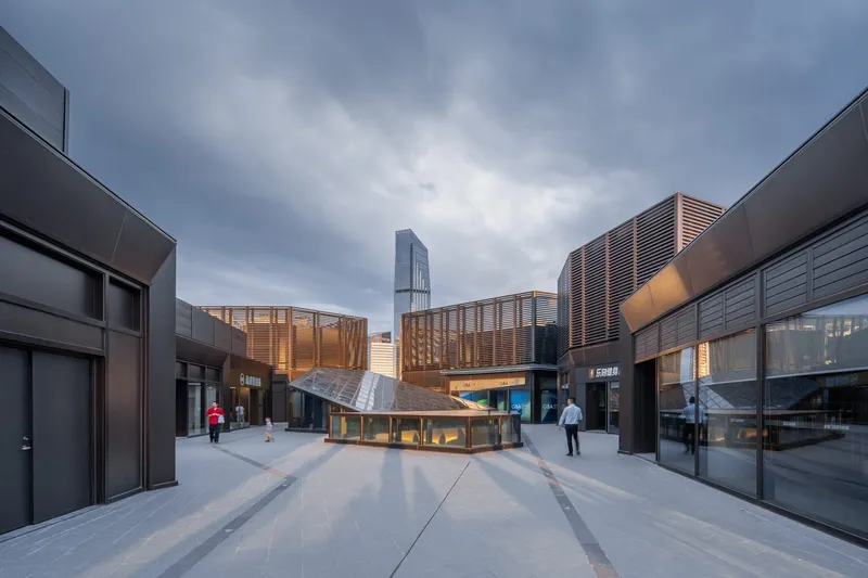 Rooftop courtyard with wooden pavilion surrounded by terracotta screens and shop fronts at dusk