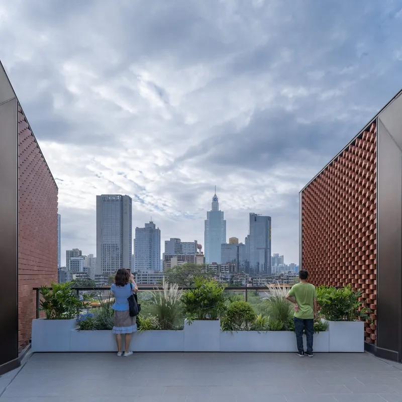 Rooftop terrace framed by terracotta screens with two visitors looking toward the city skyline under cloudy skies