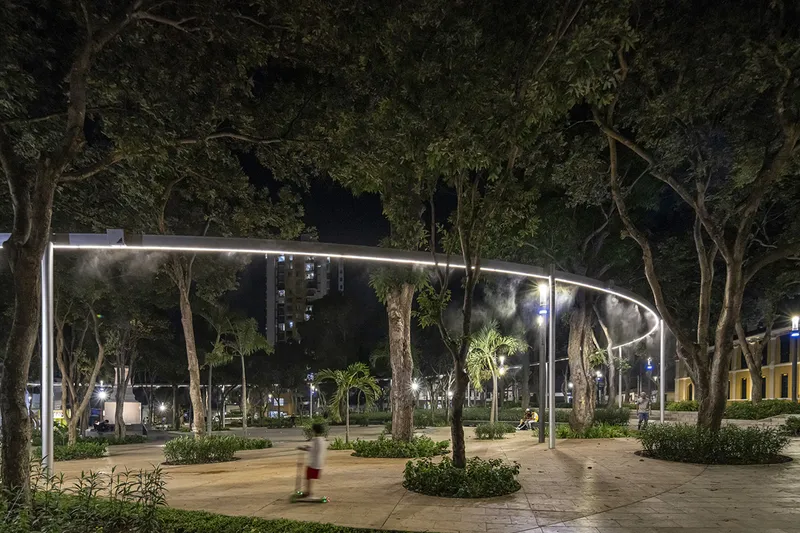 Illuminated curved tubular canopy with integrated misting system threading among the trees at night