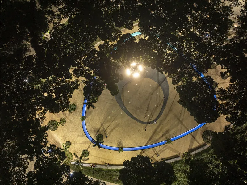 Aerial view of the circular plaza with blue curving benches among the trees at dusk