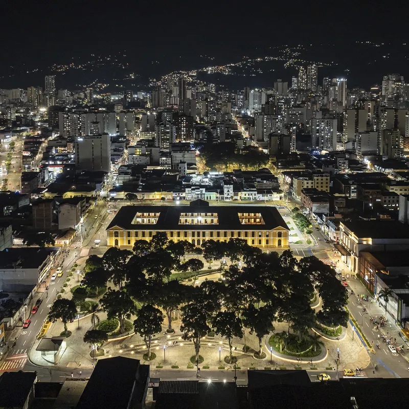 Night aerial view of the illuminated plaza and yellow arcade building surrounded by dense urban fabric
