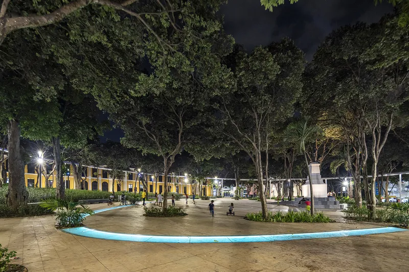 Plaza with blue curving edge and central monument framed by trees at night