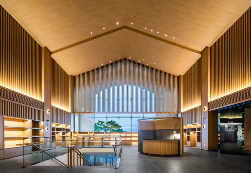 Reception lobby with vaulted timber ceiling, slatted walls, and arched window overlooking a tree