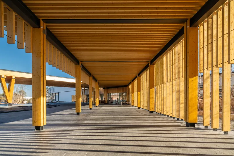 Covered walkway with timber slatted walls and ceiling casting shadow stripes on stone pavement