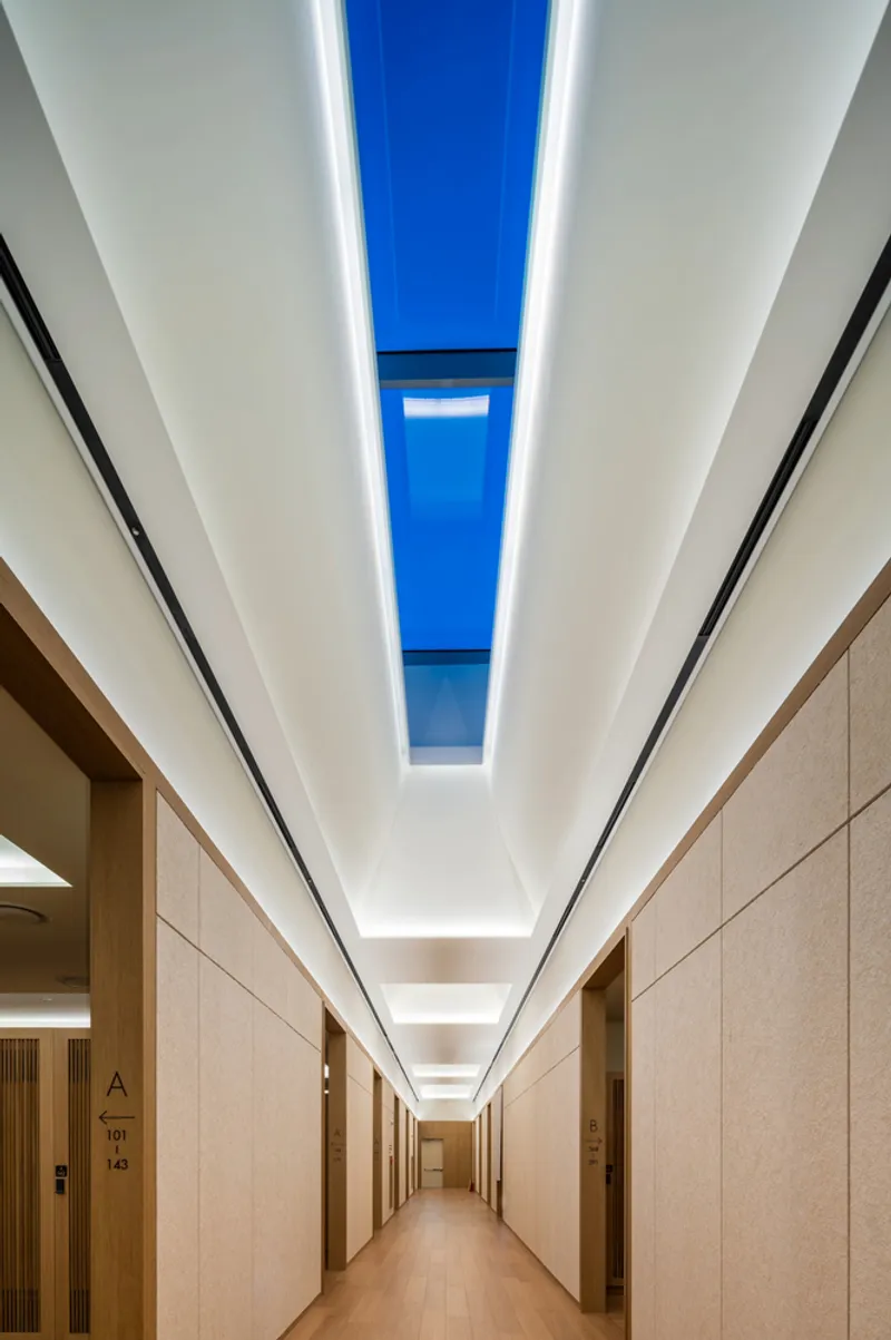 Upward view of a linear skylight with blue sky between white ceiling planes