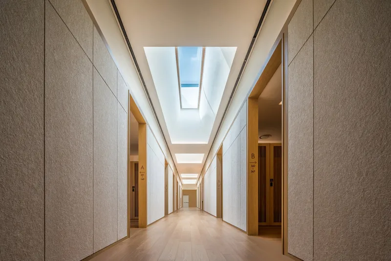 Corridor with textured stone walls and linear skylights illuminating timber doorways