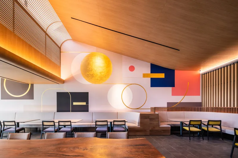 Dining hall interior with geometric wall graphics and timber-clad curved ceiling with perimeter cove lighting
