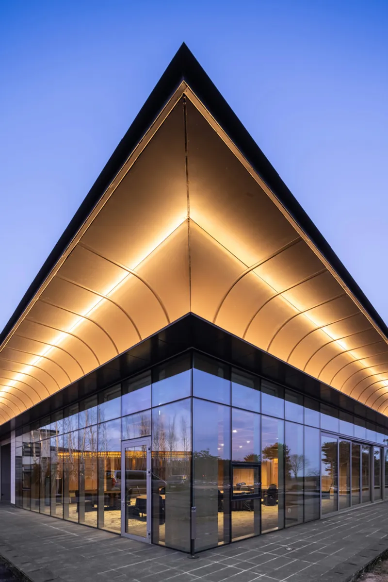 Corner view of the illuminated vaulted timber soffit above full-height glazing at twilight