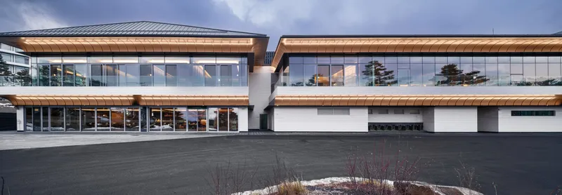 Two-storey facade with continuous glazing and timber soffits facing a courtyard with sparse planting beds