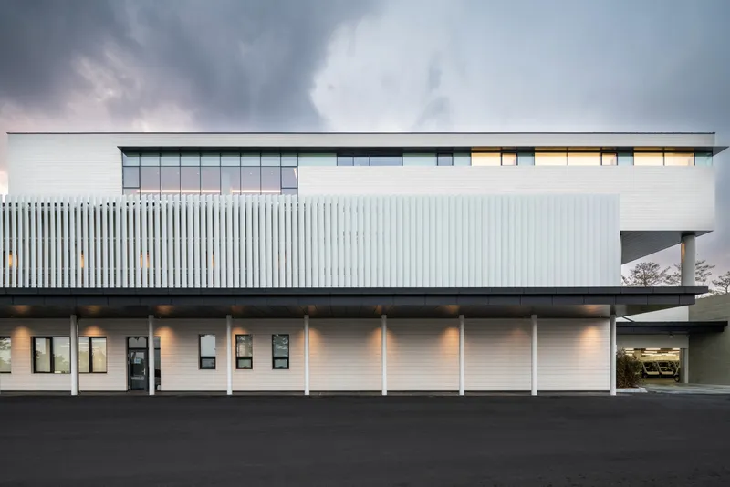 Horizontal white-paneled facade with vertical louvered screen and evenly spaced columns under a dark sky