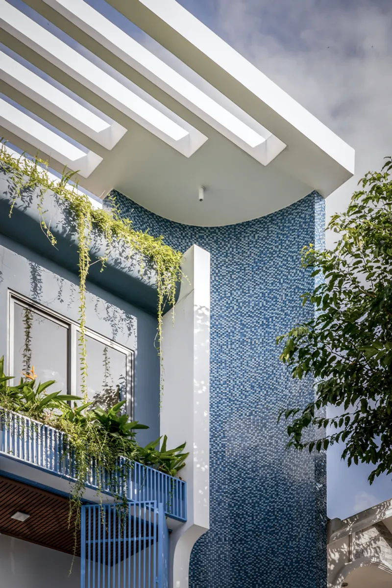 Interior courtyard with blue mosaic tile column, slatted overhang, and cascading greenery under open sky