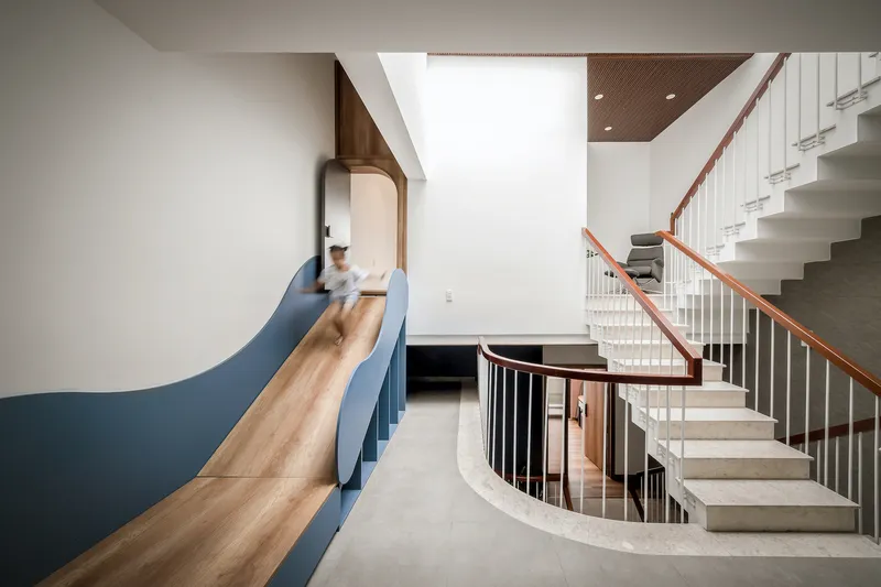 Multi-level stairwell with timber-edged slide alongside concrete stairs and a person in motion blur