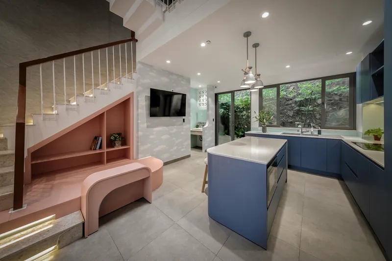 Open-plan kitchen and living area with blue island, pink niche shelving, and garden view