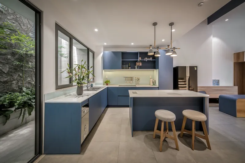 Open kitchen with navy blue cabinetry and white marble countertops overlooking a planted courtyard through floor-to-ceiling glazing